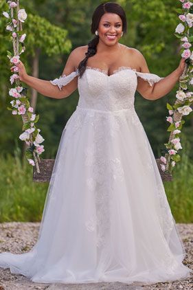 Woman in a white lace wedding dress standing between flower-covered arches in a garden setting
