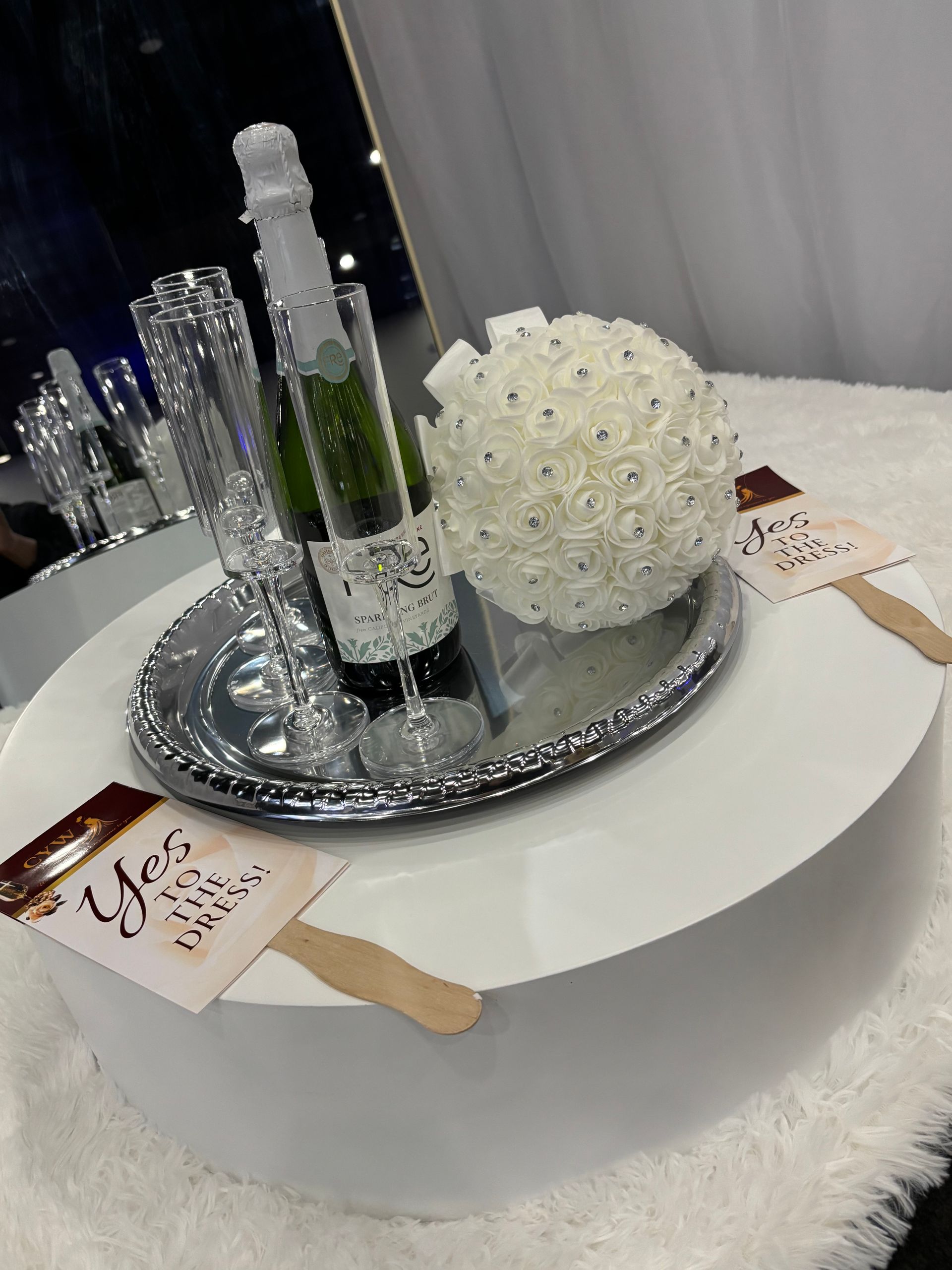 Decorated white table with champagne bottle, glasses, silver tray, and white floral centerpiece