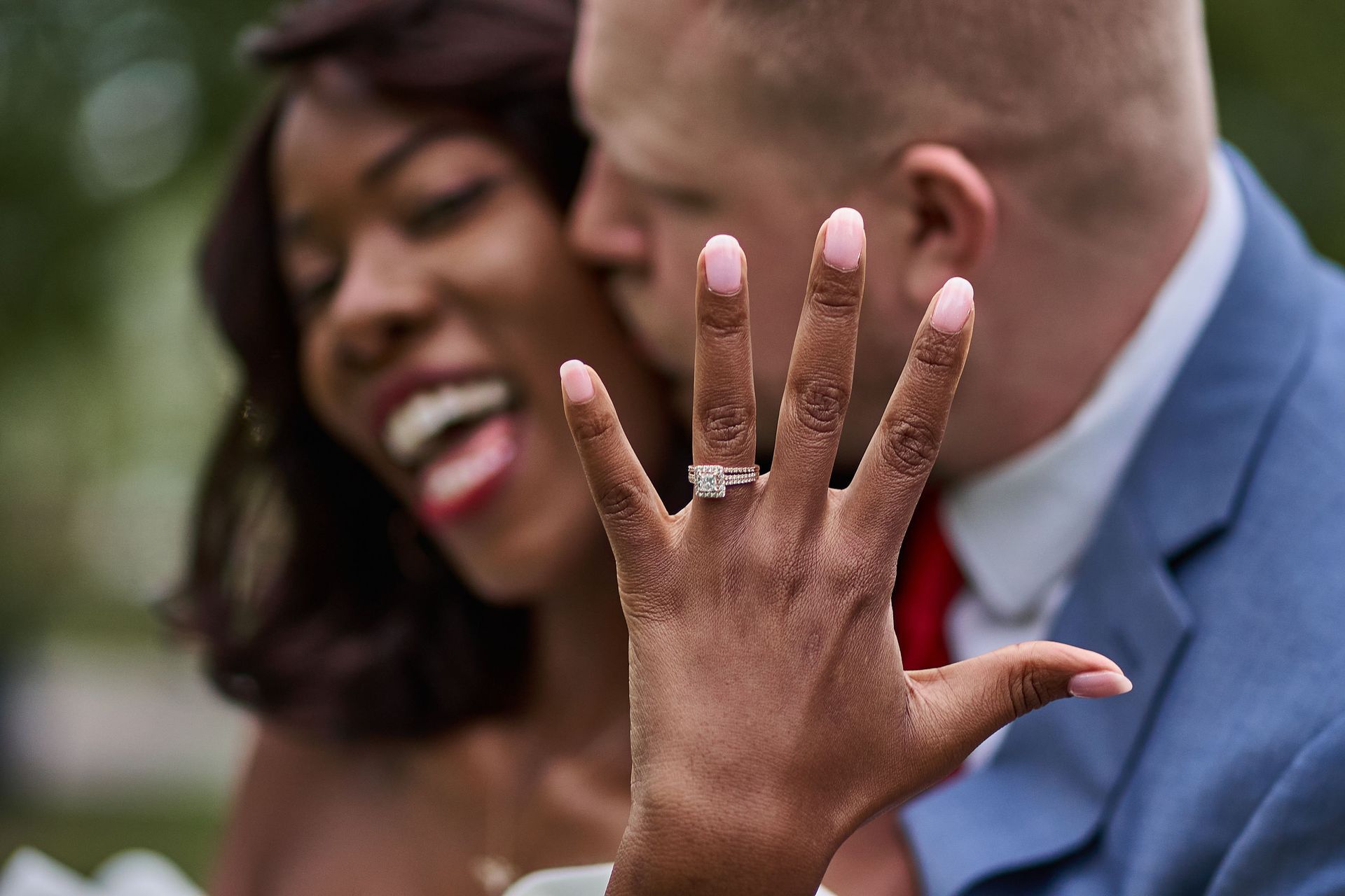 Smiling couple outdoors, with a hand showing a ring in the foreground