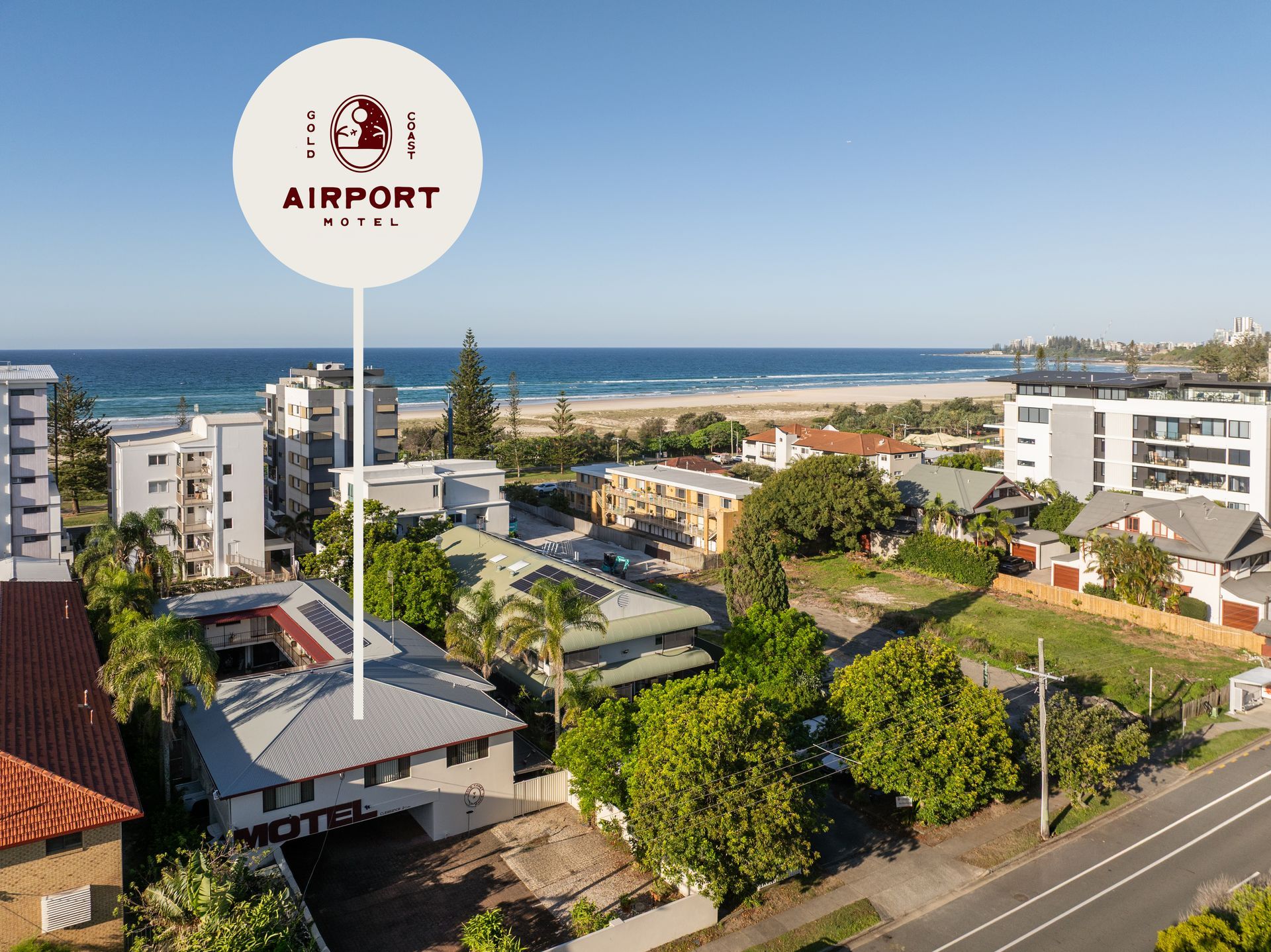 Coastal neighborhood with airport sign, buildings, trees, and ocean in the background
