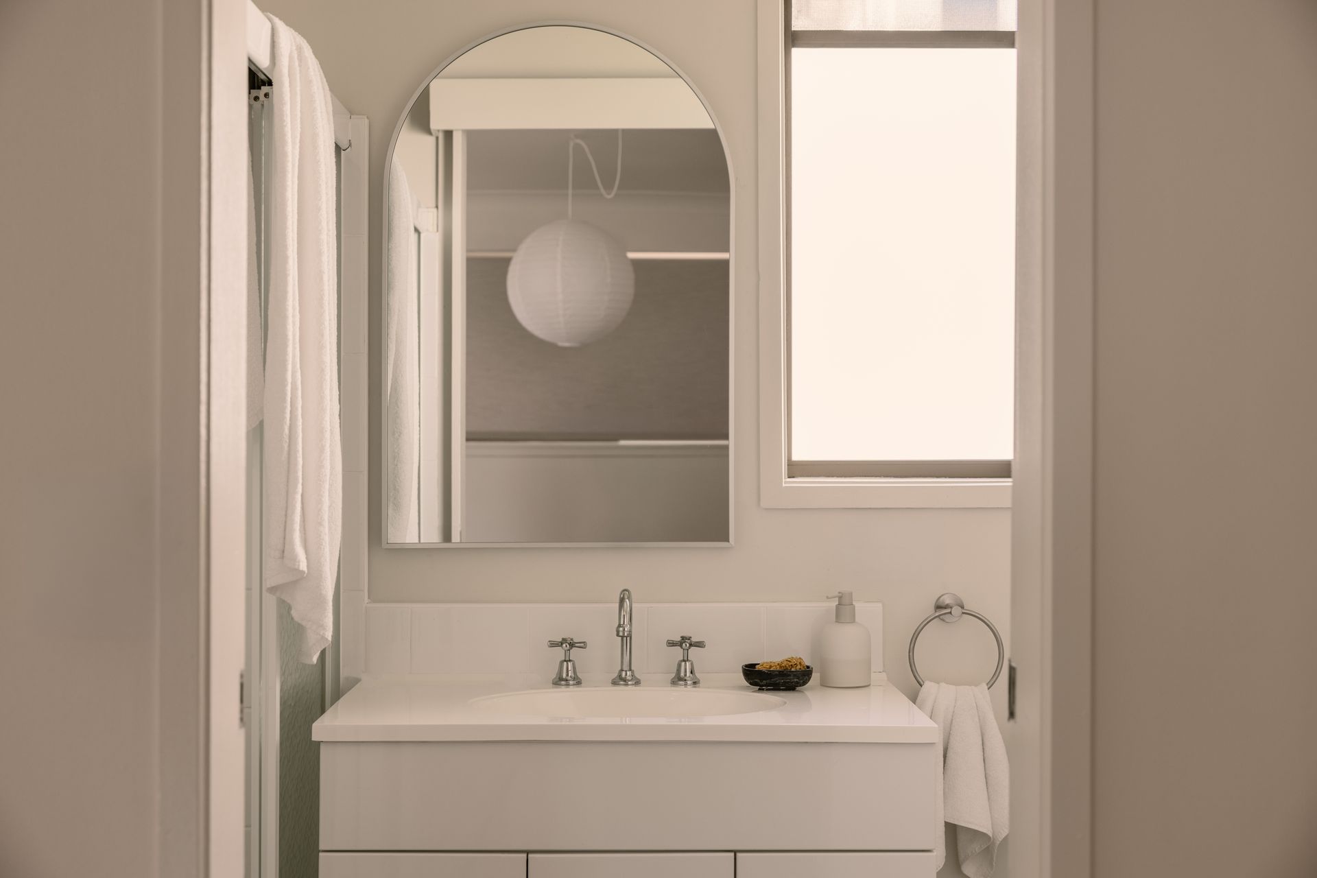 Minimalist bathroom with white vanity, mirror, towels, and soft beige walls
