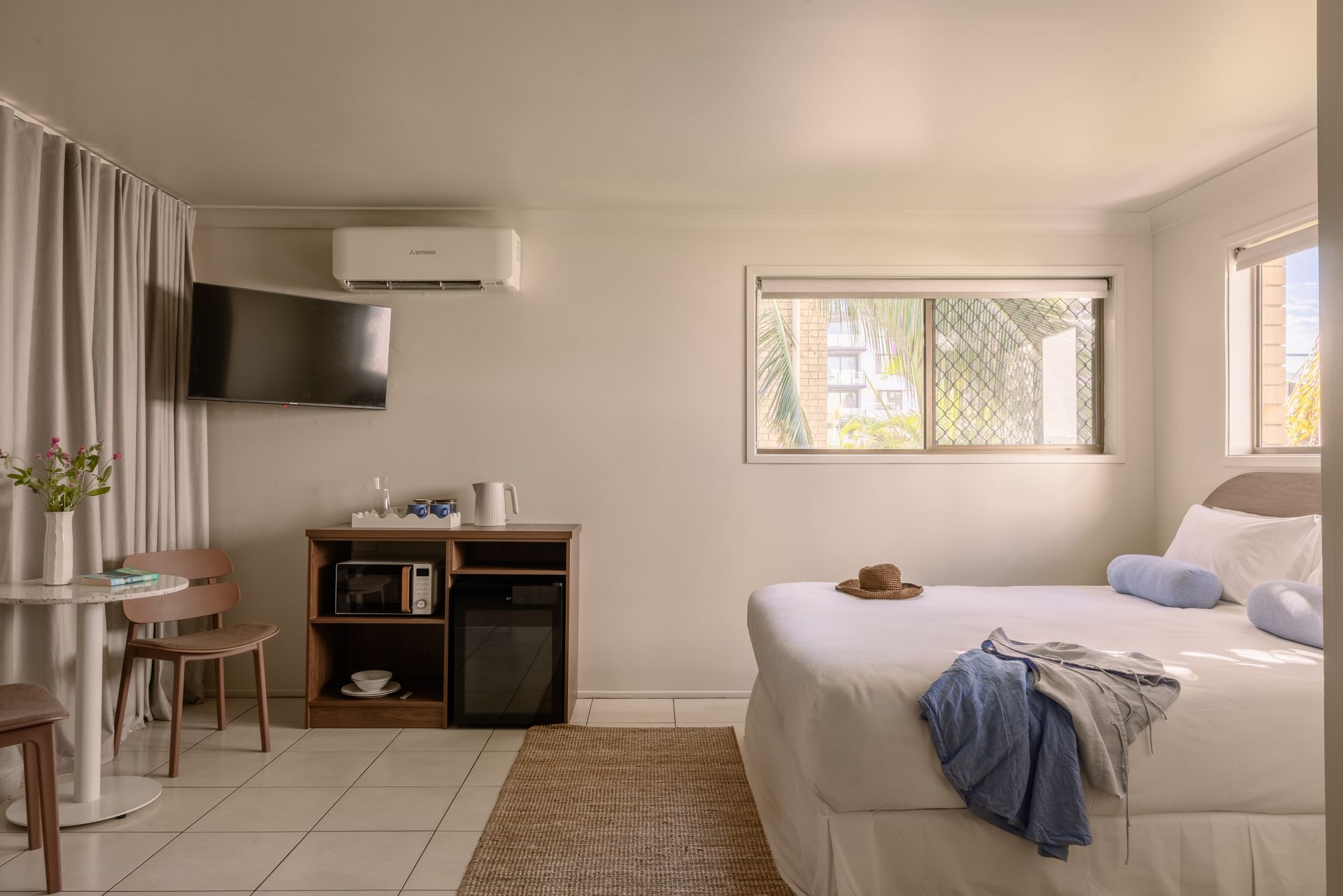 Neat bedroom with bed, desk, wall TV, curtains, and soft beige decor.