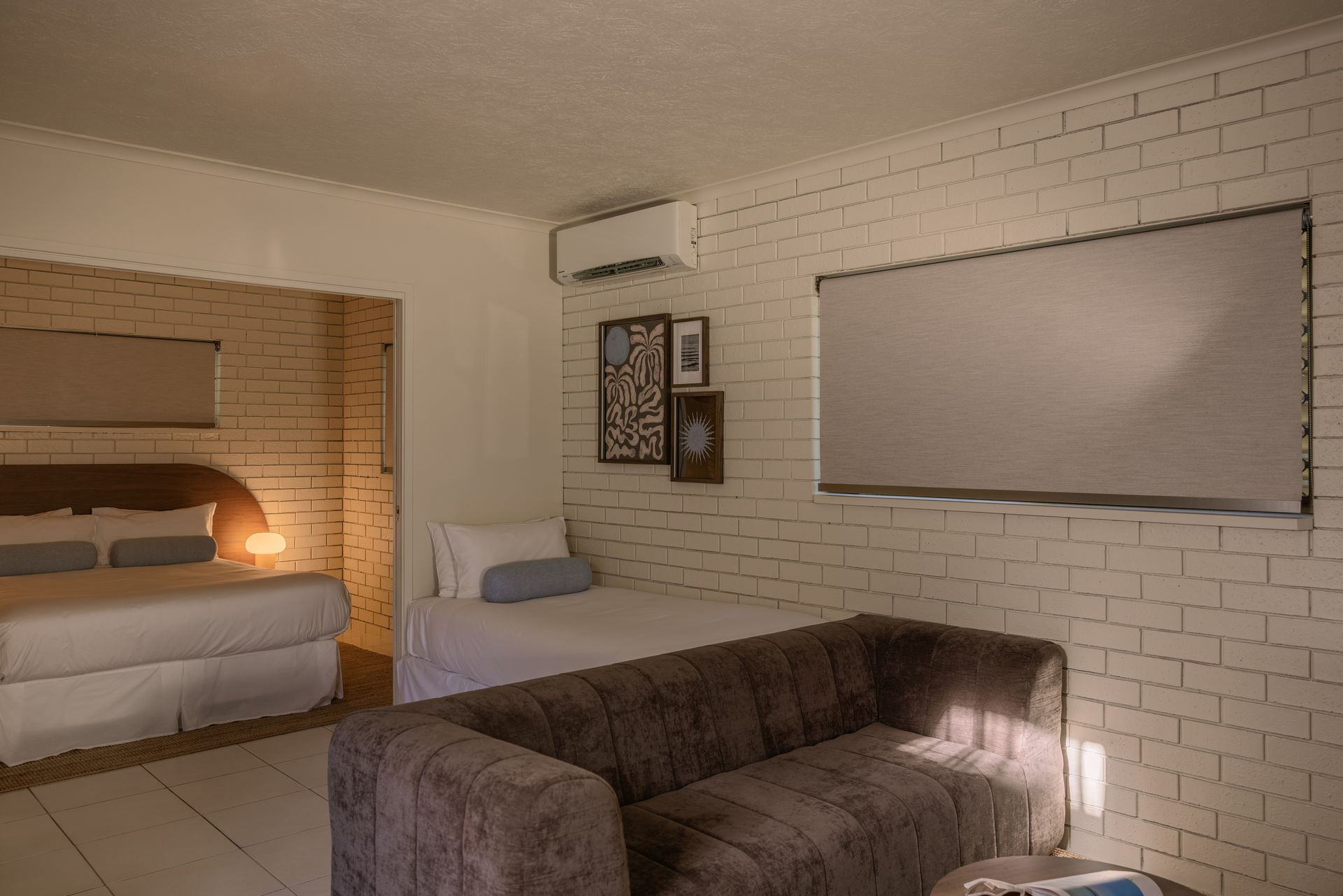 Cozy bedroom with a bed, couch, lamp, and framed wall art in warm beige tones