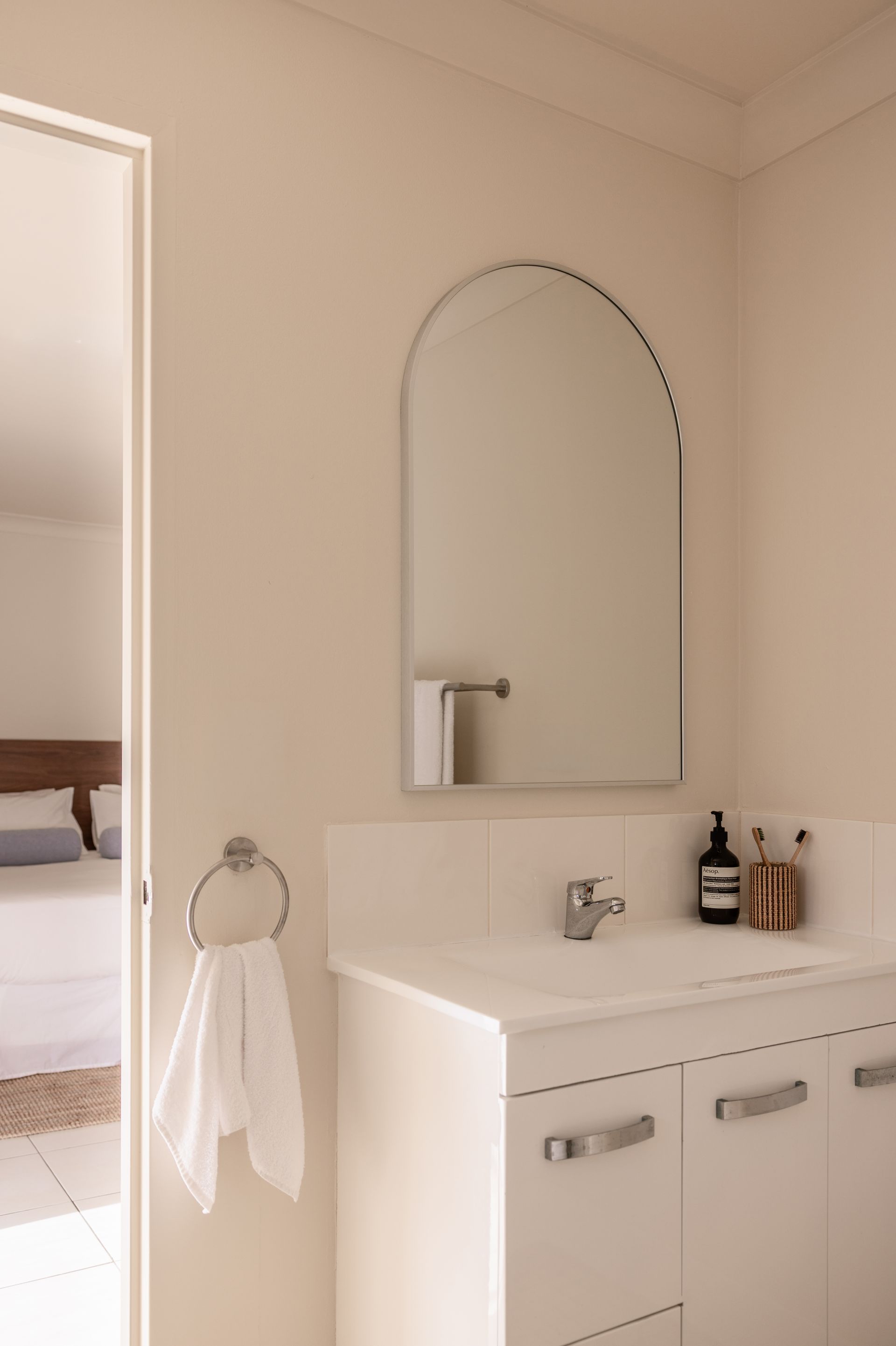 Small white bathroom vanity with arched mirror, towel ring, and sink against beige walls