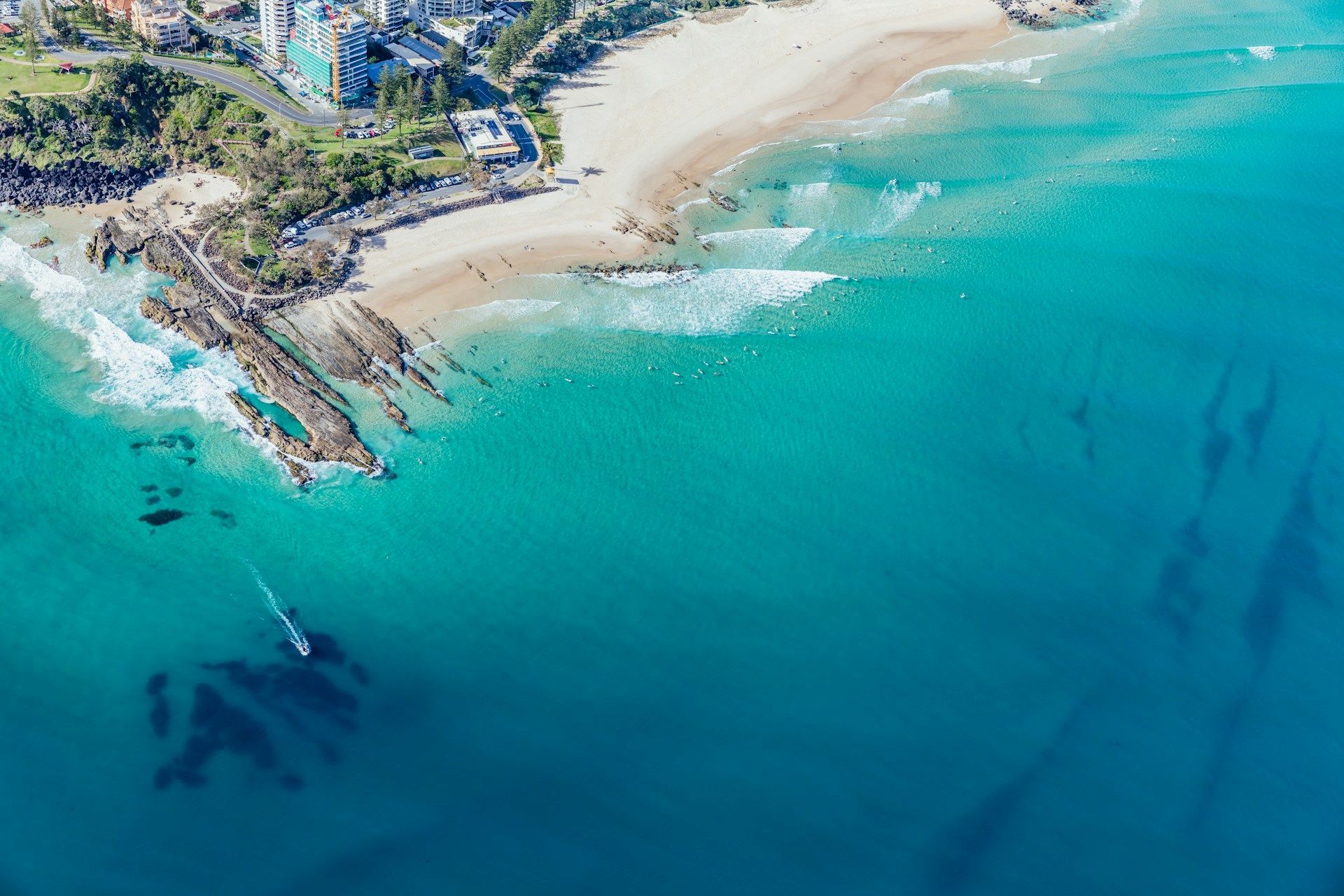 Aerial view of a sandy beach with turquoise waves, rocky shoreline, and coastal homes on a sunny day