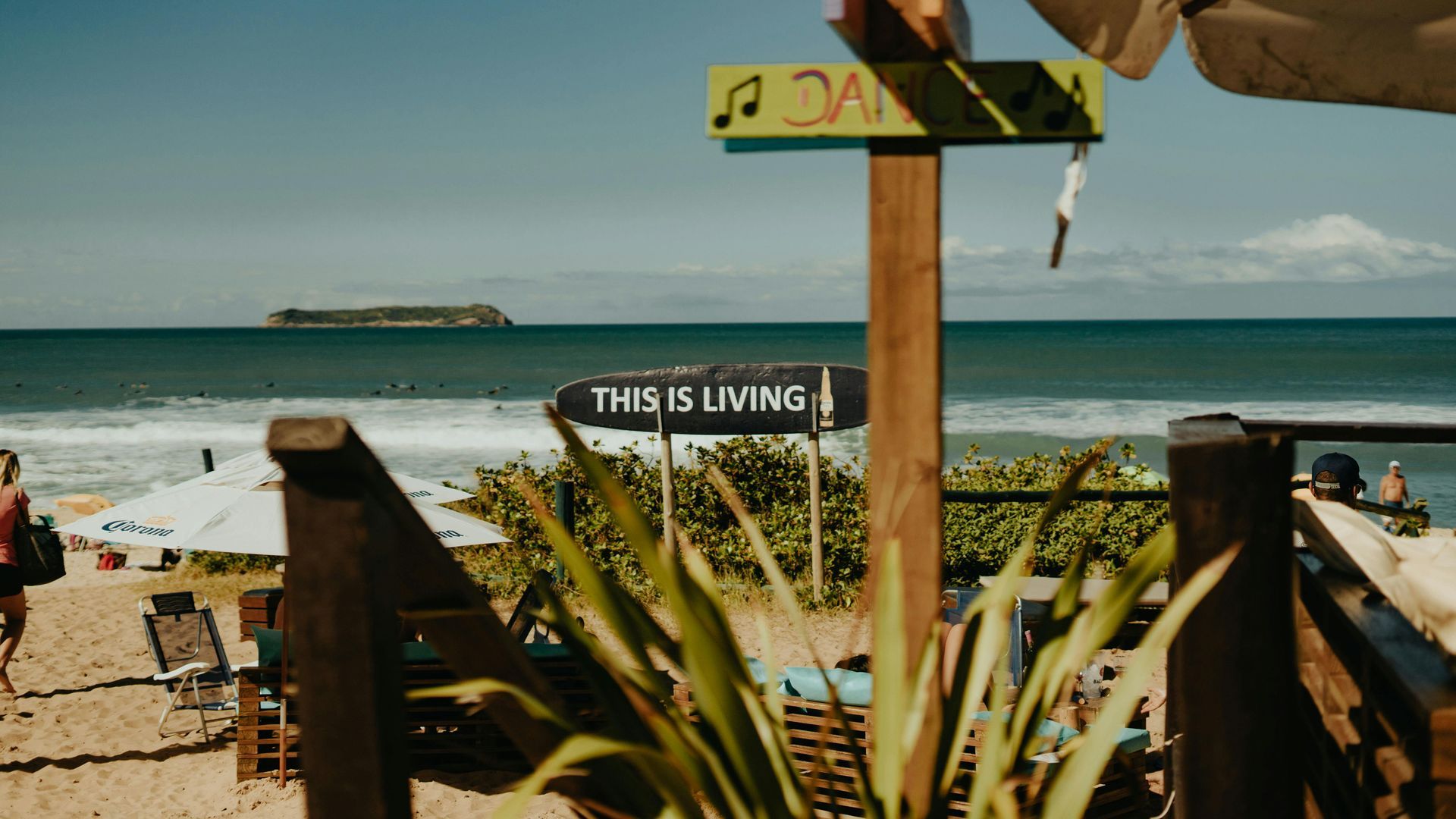 Beachfront view with signpost, surfboards, and ocean waves under a clear sky