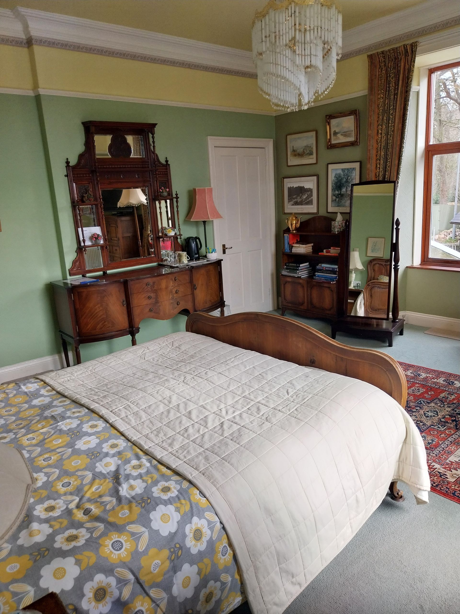 A vintage-style bedroom with green walls, a patterned bedspread, wooden furniture, and a crystal chandelier.