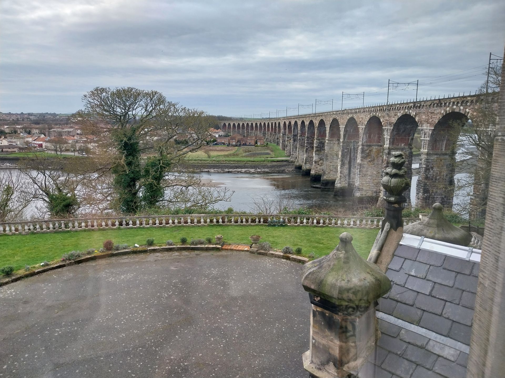 A stone viaduct stretches across a river, viewed from a high vantage point overlooking a paved circular driveway.
