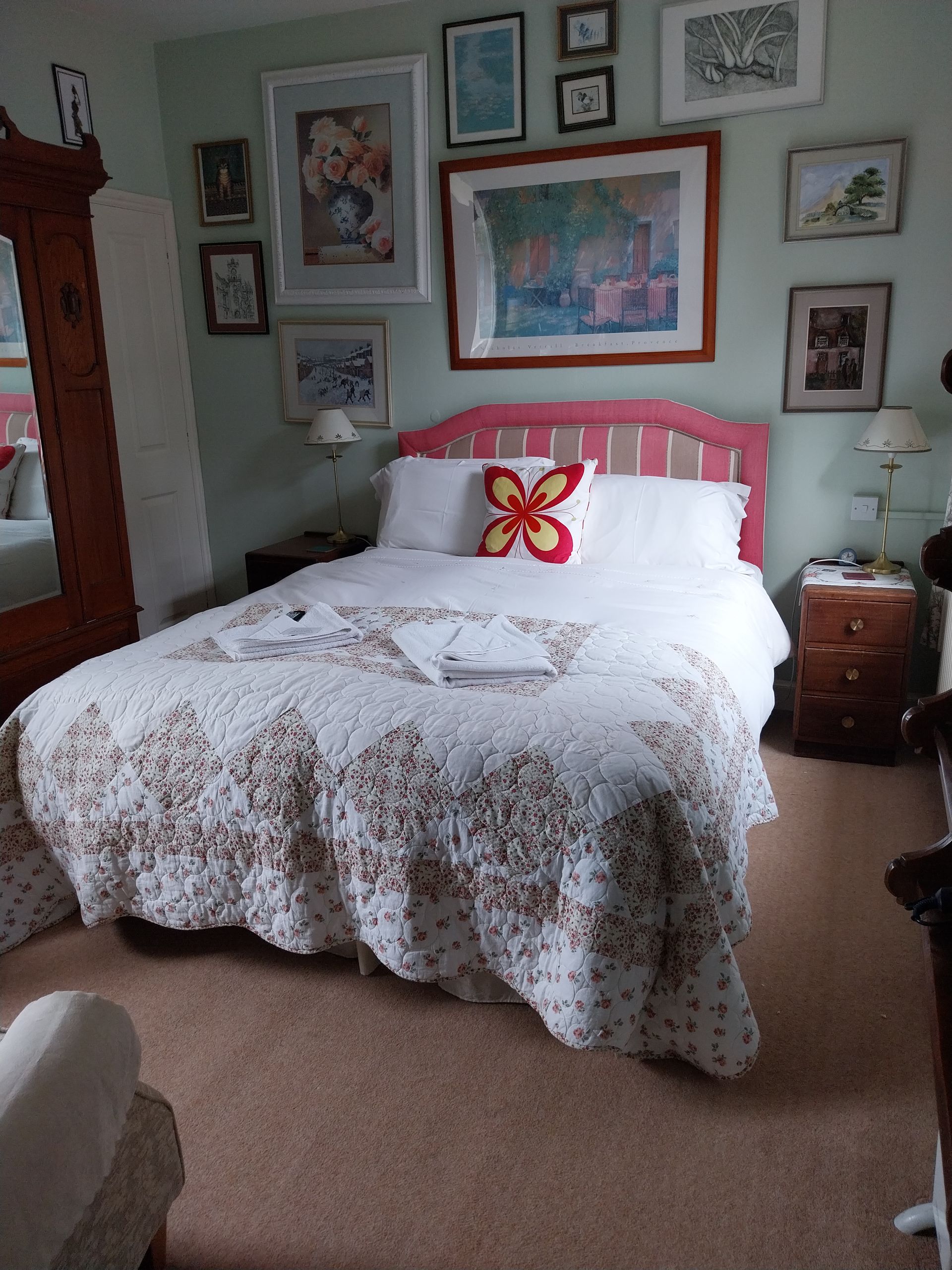 A bedroom with a bed featuring a pink headboard and floral quilt, surrounded by a gallery wall of framed art.