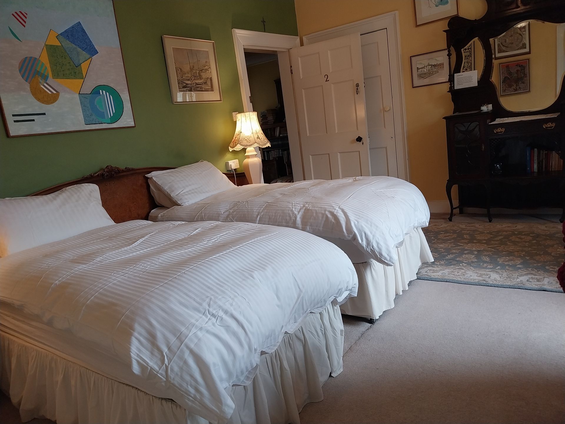 A bedroom with two twin beds featuring white bedding, an olive-green accent wall, and an antique vanity mirror.