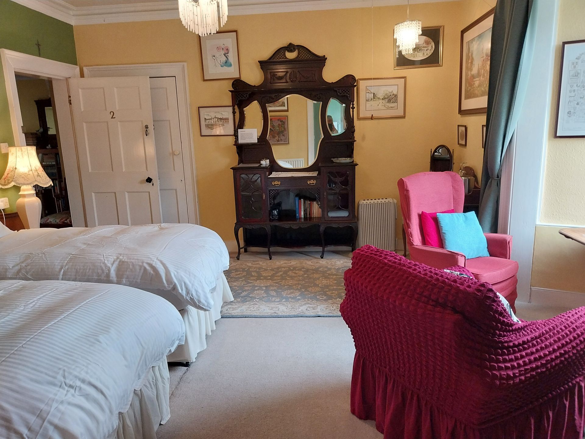 Room with two white-bedded twin beds, a dark wood dresser with a mirror, and two pink armchairs with colourful pillows.