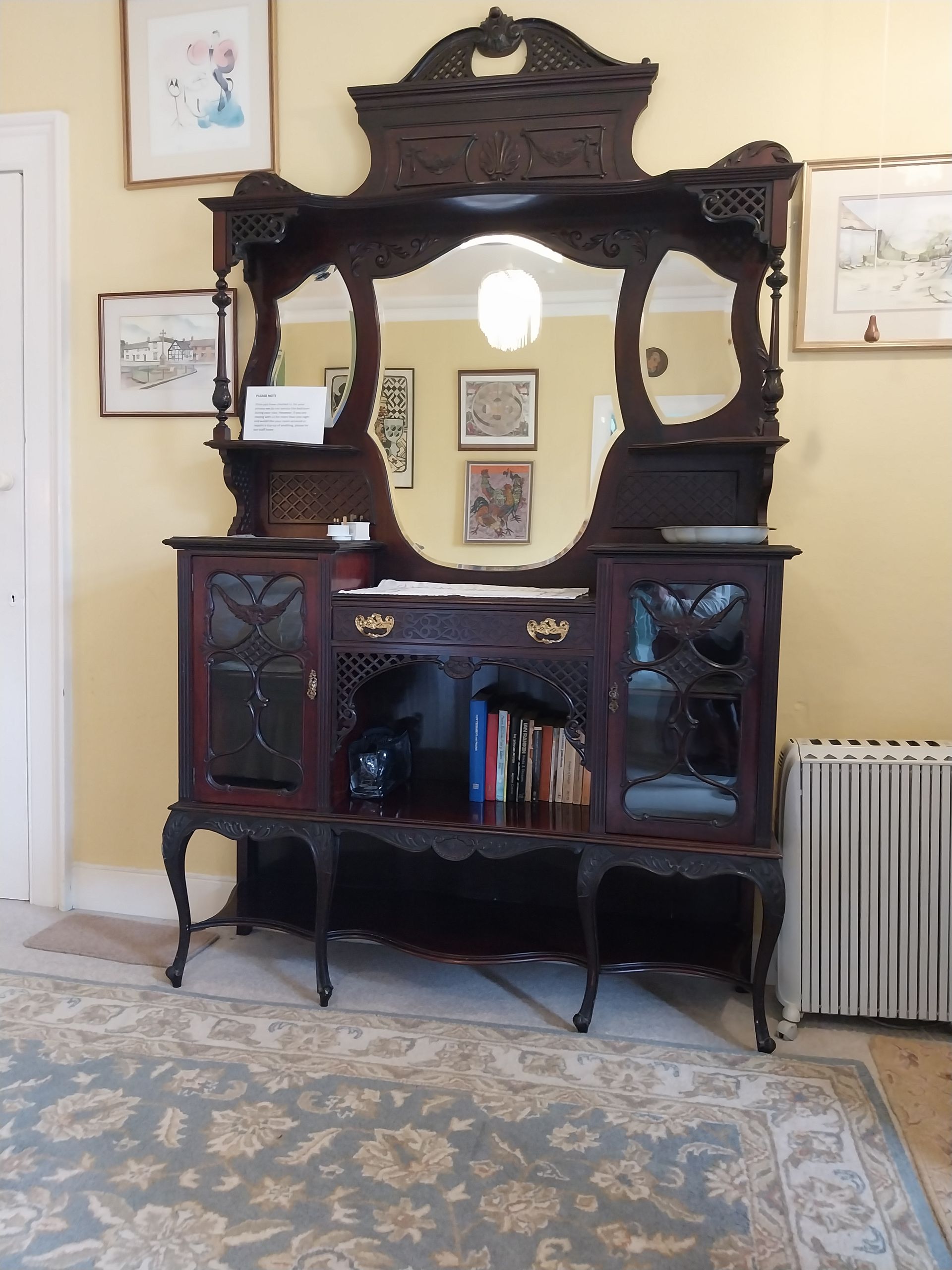 An ornate, dark wood antique sideboard with a large central mirror, glass-paned doors, and shelving, set in a room.