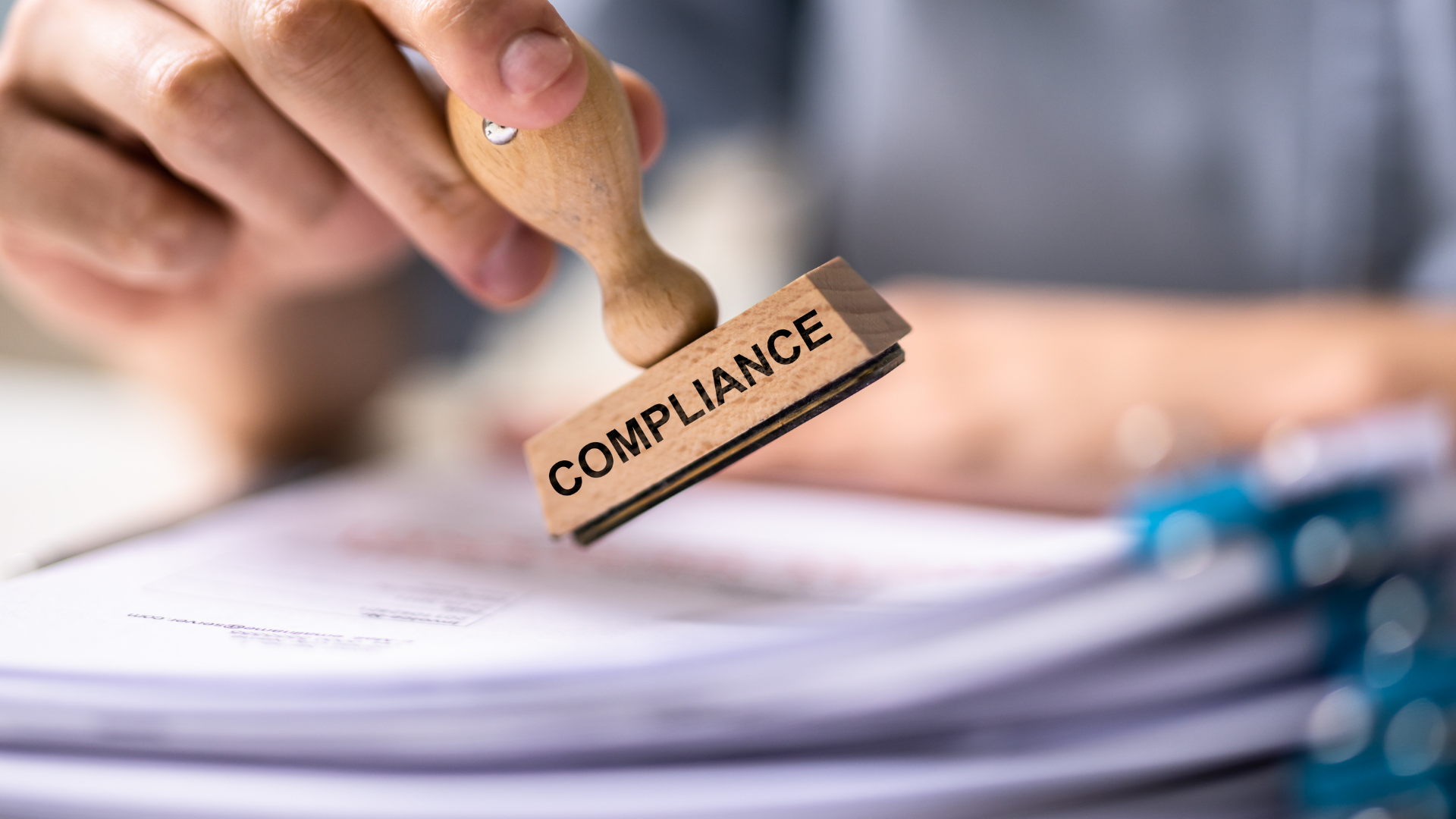 Hand stamping “COMPLIANCE” on paperwork with a wooden rubber stamp