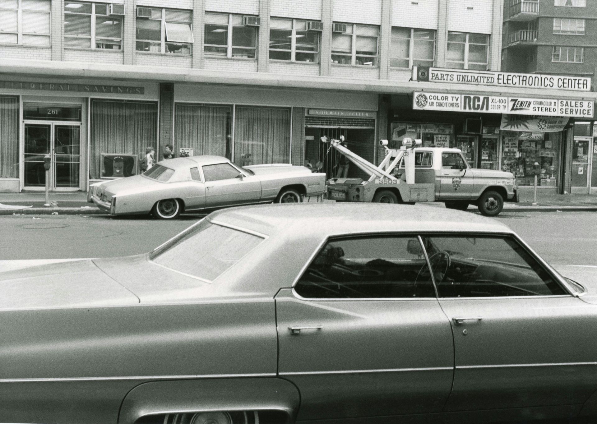 A black and white photo of a car parked in front of a building that says one way