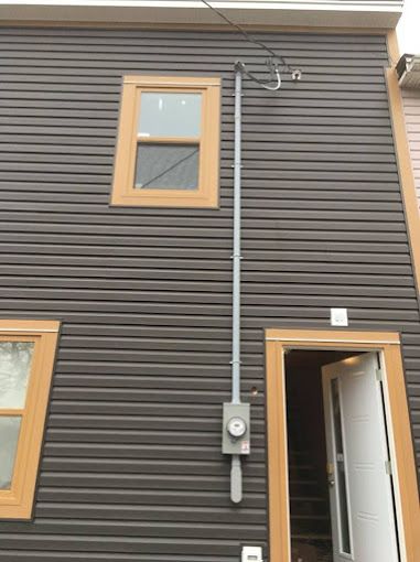 Exterior wall of a house with a utility meter, conduit, windows, and an open door