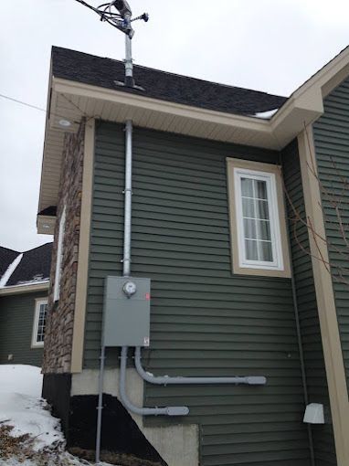 Side of a house with gray siding, electrical meter box, and conduit pipes in snowy weather