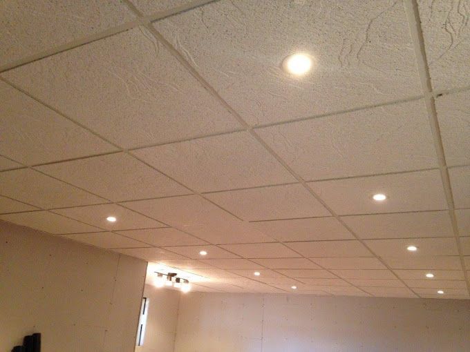 Drop ceiling with recessed lights in a beige room, viewed upward.