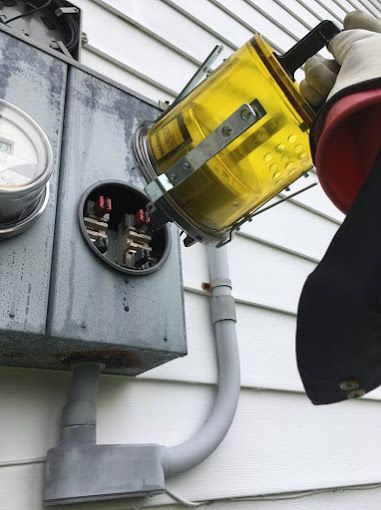 Electric meter being inspected with a handheld yellow meter reader beside a house siding