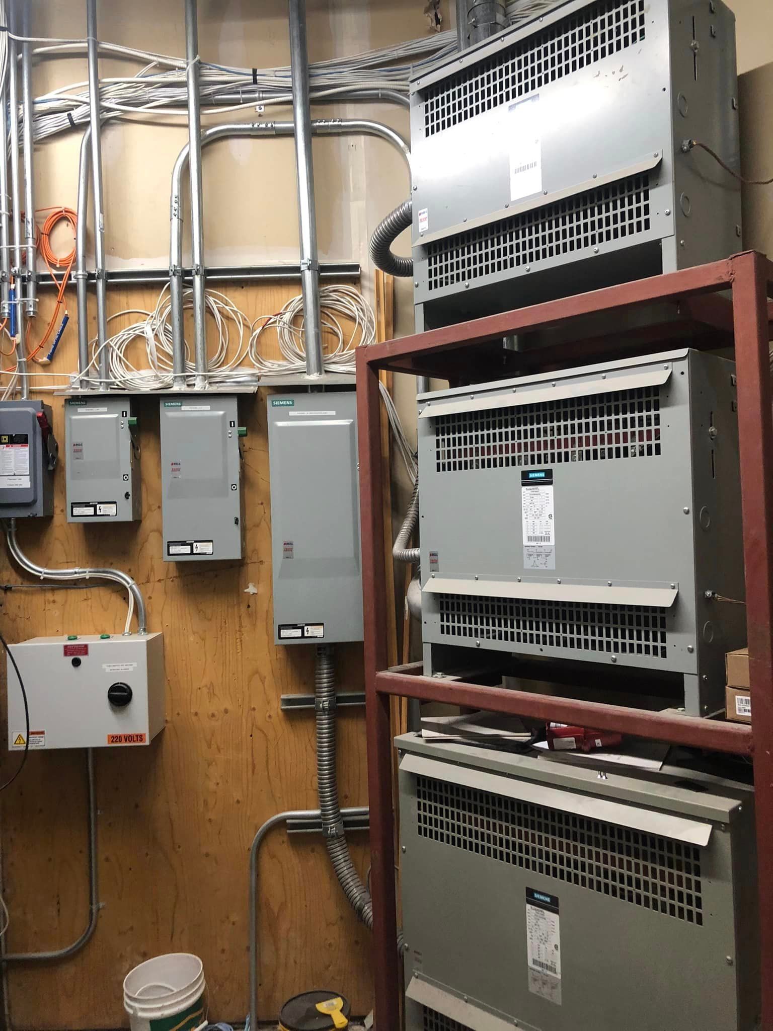 Industrial electrical control panels and wiring mounted on a plywood wall in a utility room.