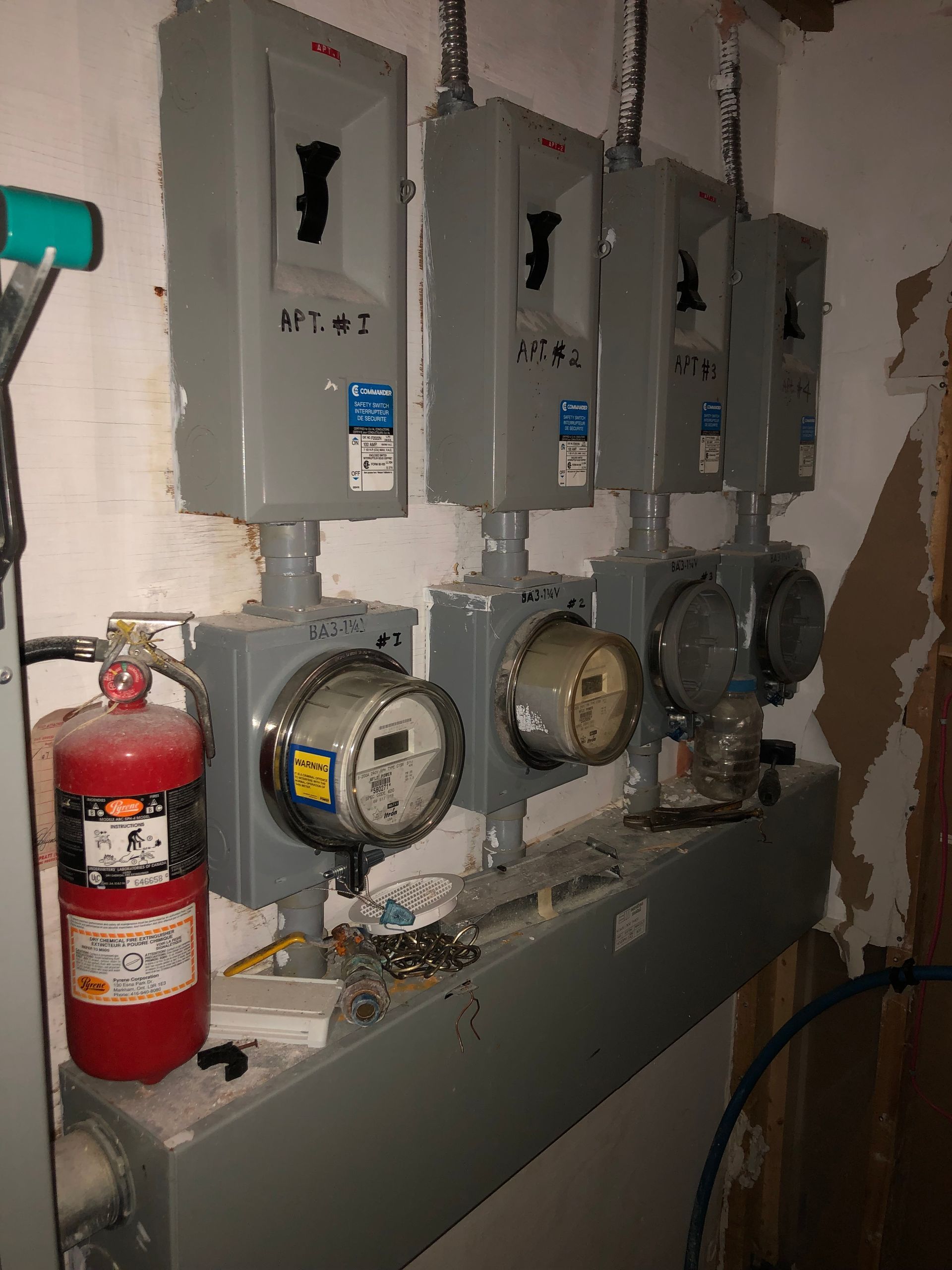 Row of utility meters and electrical panels on a wall beside a red fire extinguisher