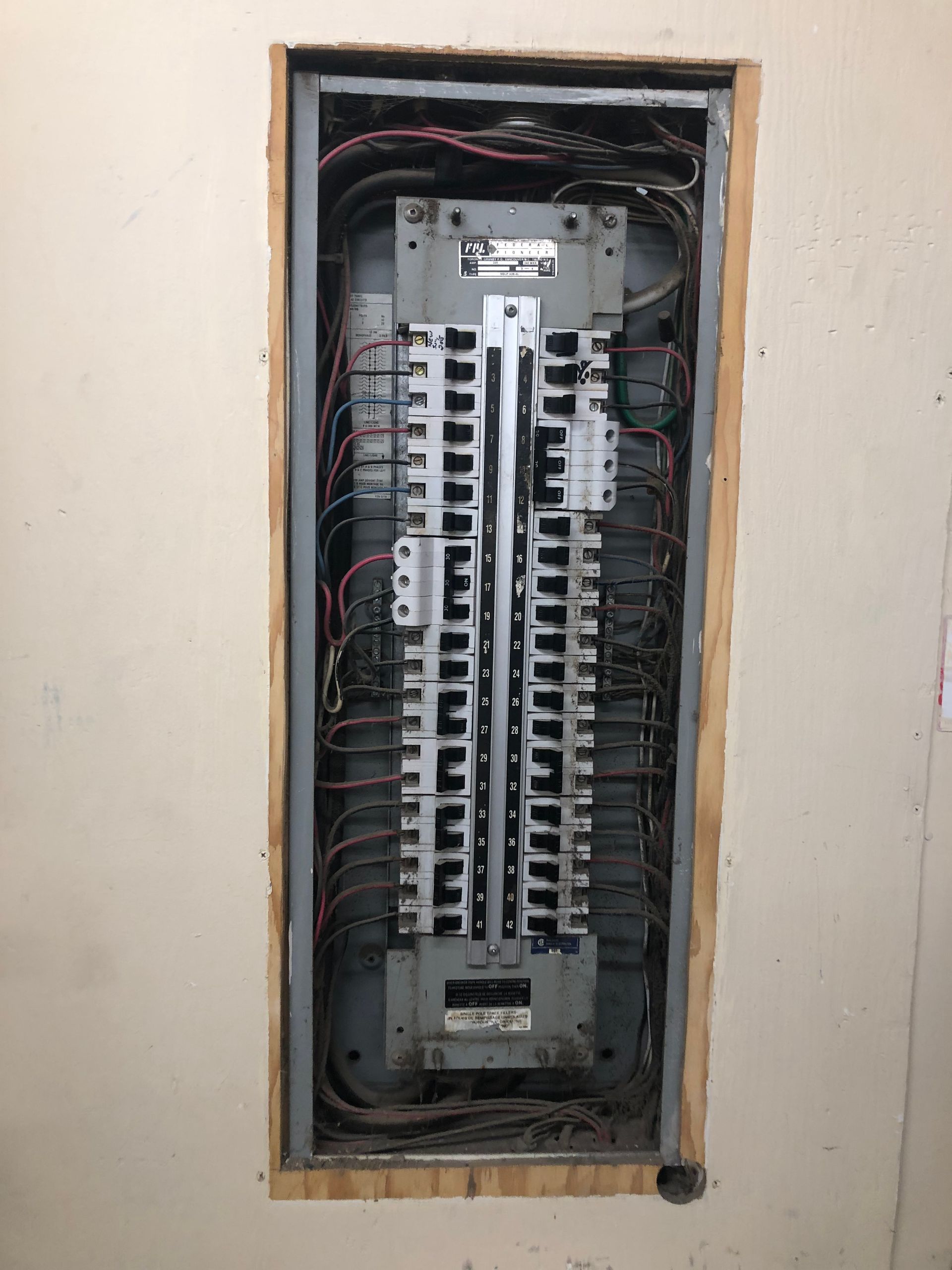 Open electrical breaker panel in a wall recess with exposed wiring and switches