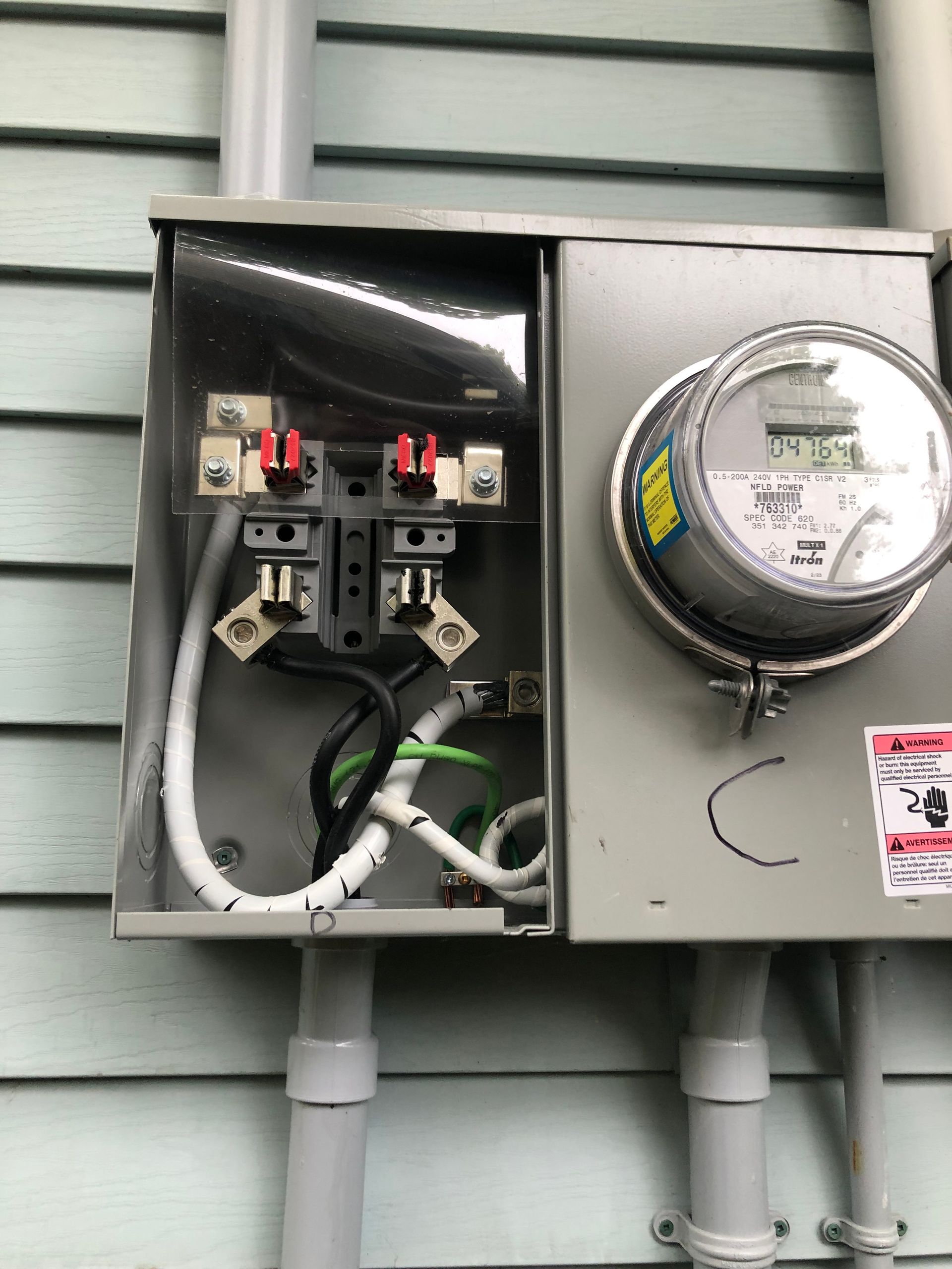 Open electrical meter and breaker box on an exterior wall with conduits and wires