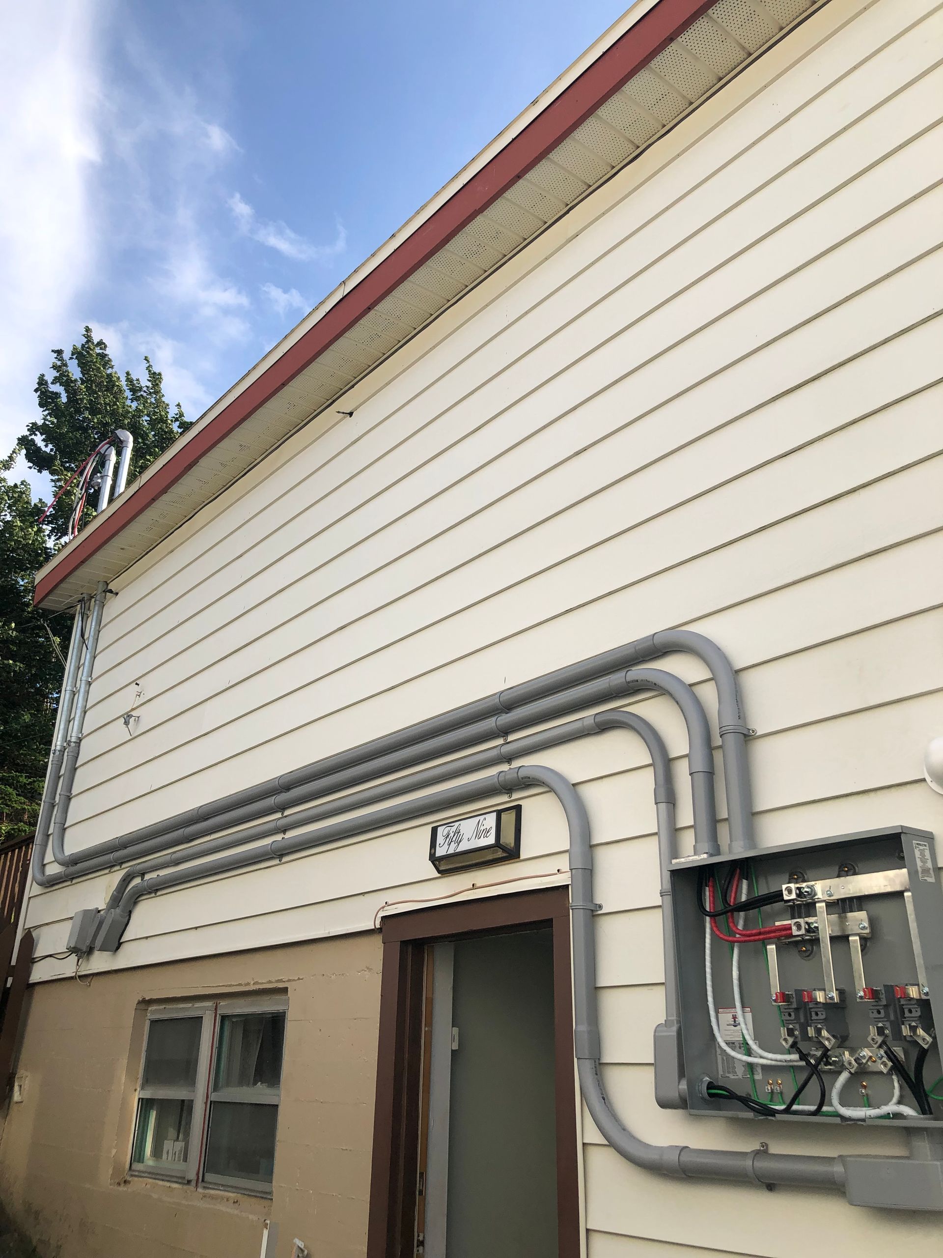 Exterior wall with beige siding, utility conduits, and an open electrical panel under a blue sky