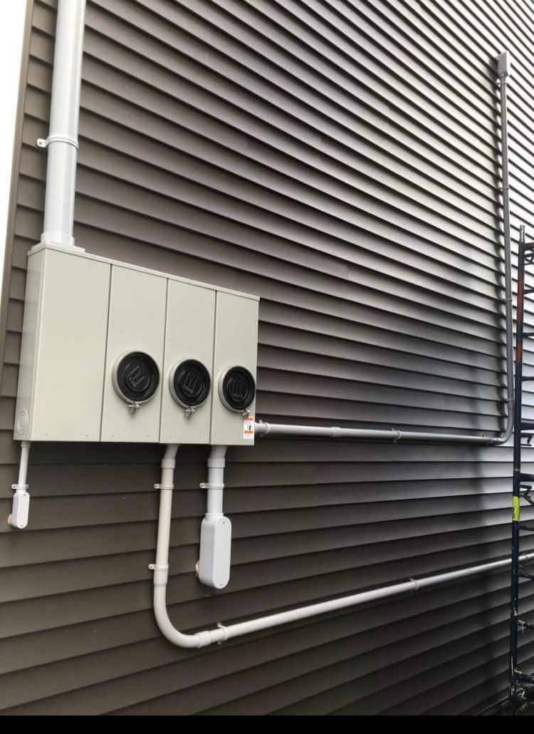 Exterior wall-mounted electrical control box with three round dials and white conduit on brown siding
