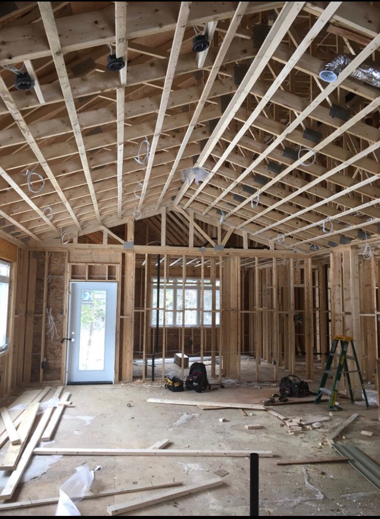 Interior of a house under construction with exposed wooden framing, trusses, and scattered tools on the floor.