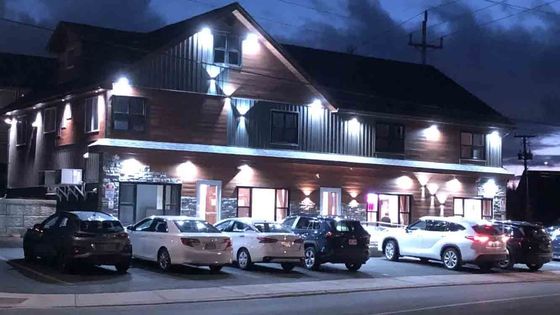 Snowy evening outside a lit two-story building with parked cars along the street.