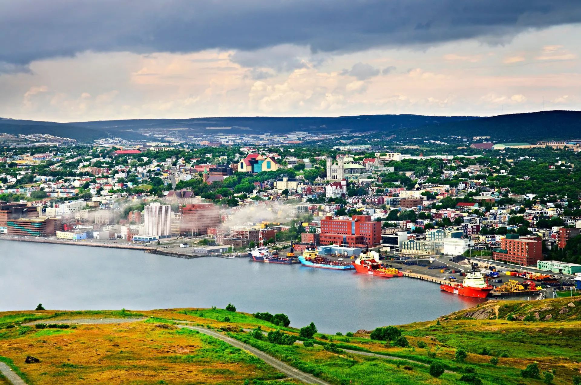 Wide view of a coastal city and harbor with colorful buildings under a cloudy sky