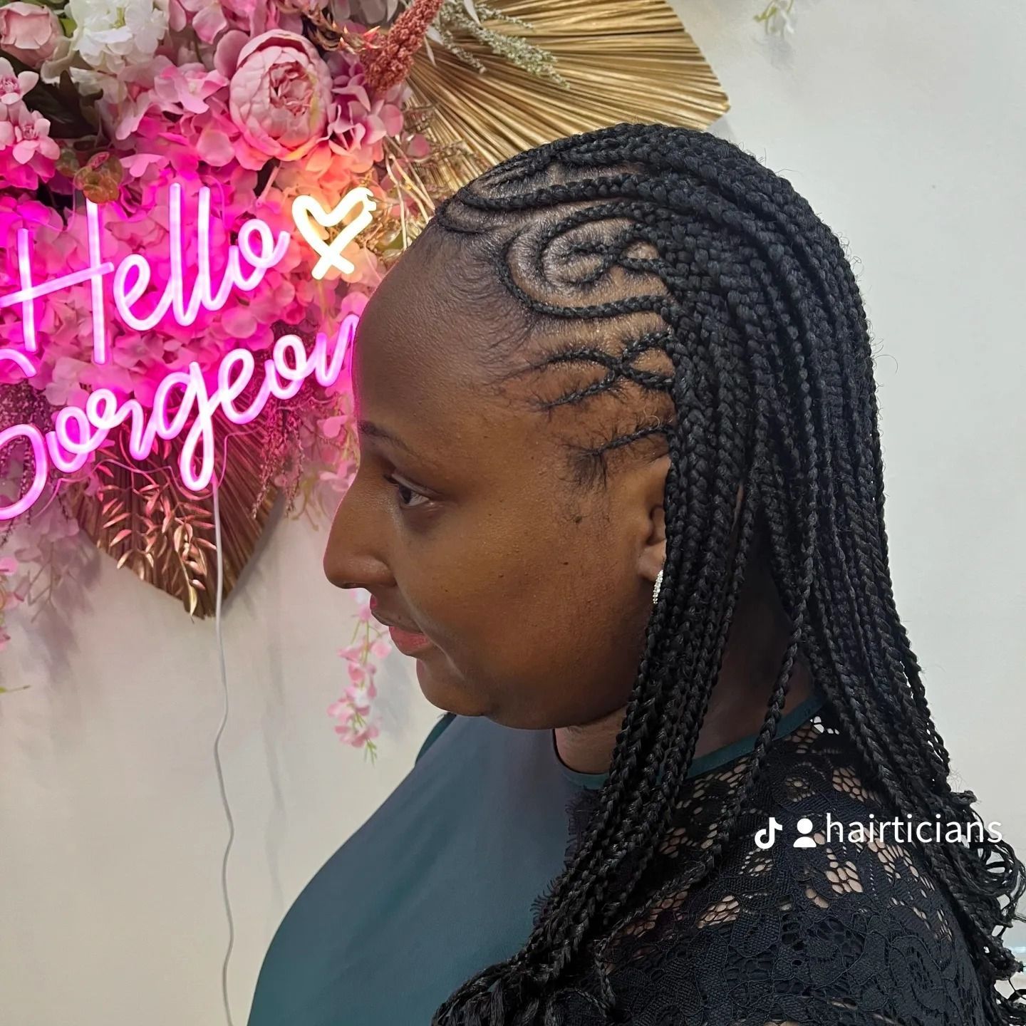 Side-profile portrait of a woman with braided hair beside a pink “Hello Gorgeous” neon sign.