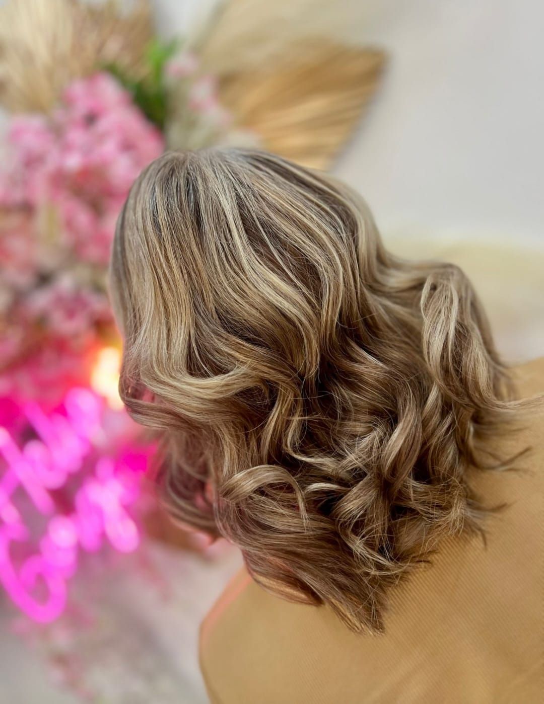 Short wavy blonde-highlighted hairstyle shown from the back, with a pink floral background