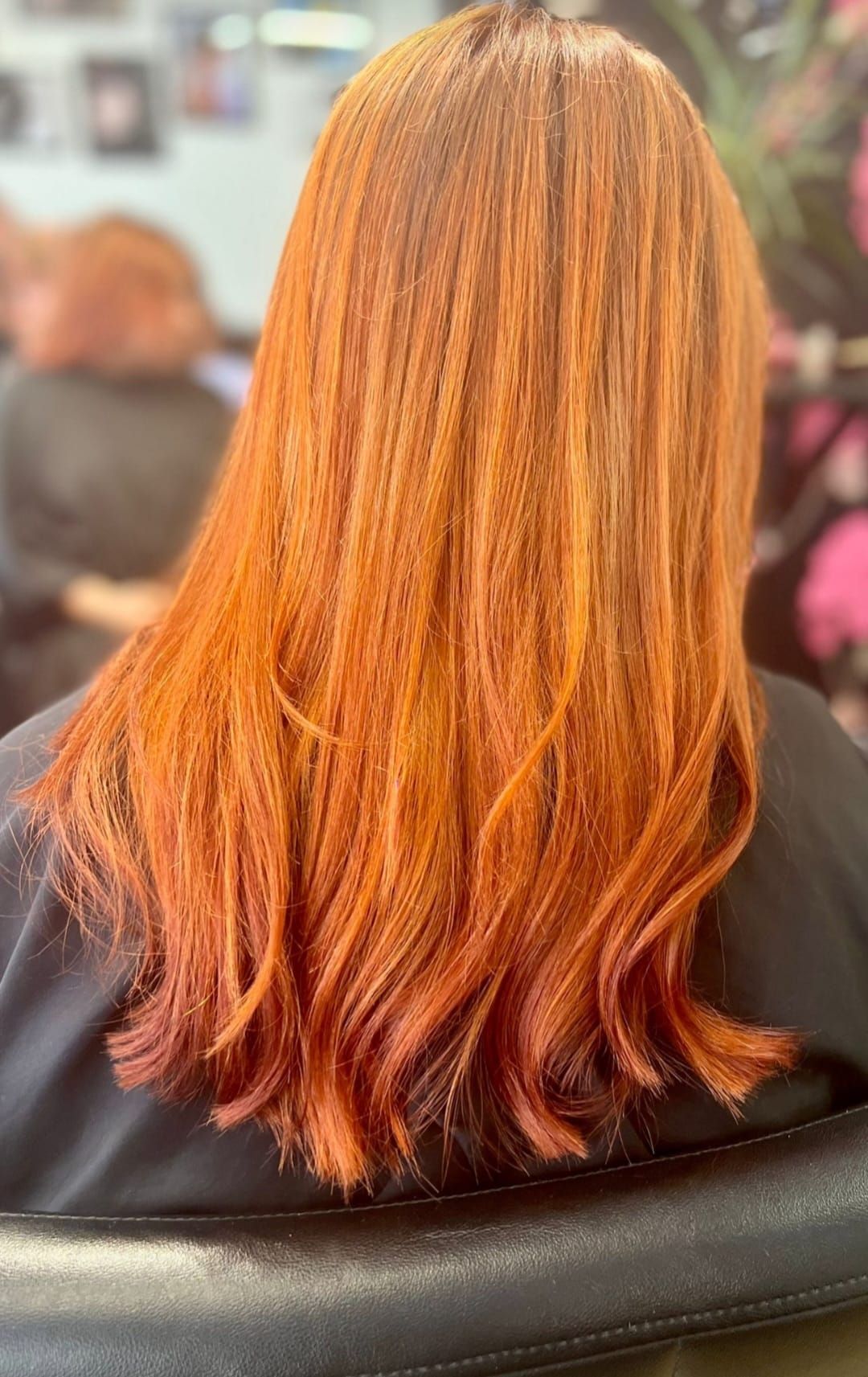 Long layered orange-red hair viewed from behind in a salon chair