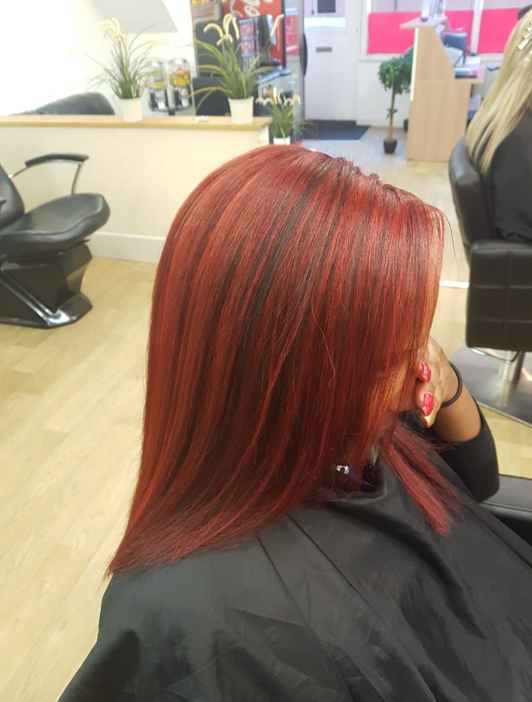 Close-up of a salon client with sleek red hair and black cape, seated in a hair salon.