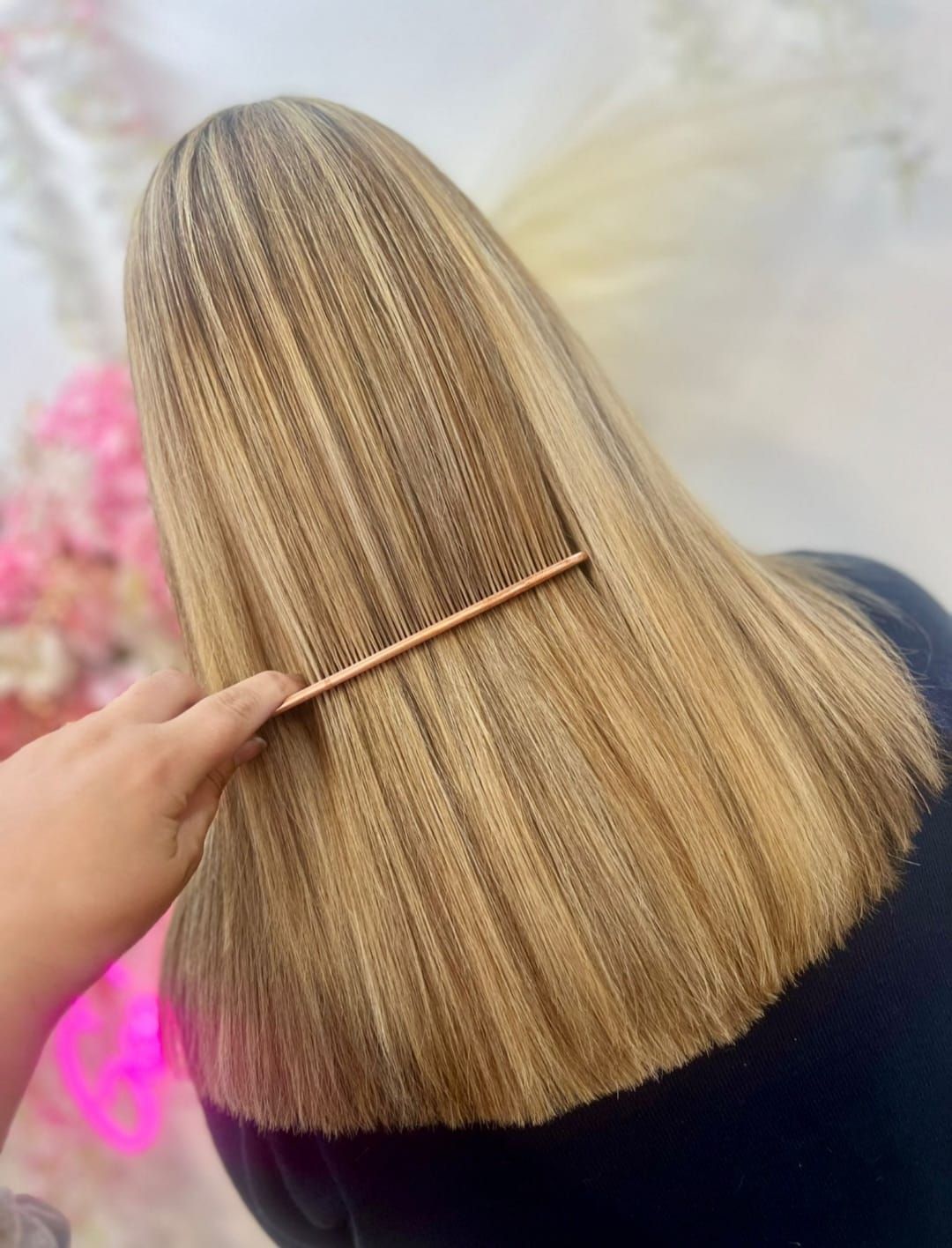 Hand holding a comb against straight, layered blonde hair with darker roots in a salon setting