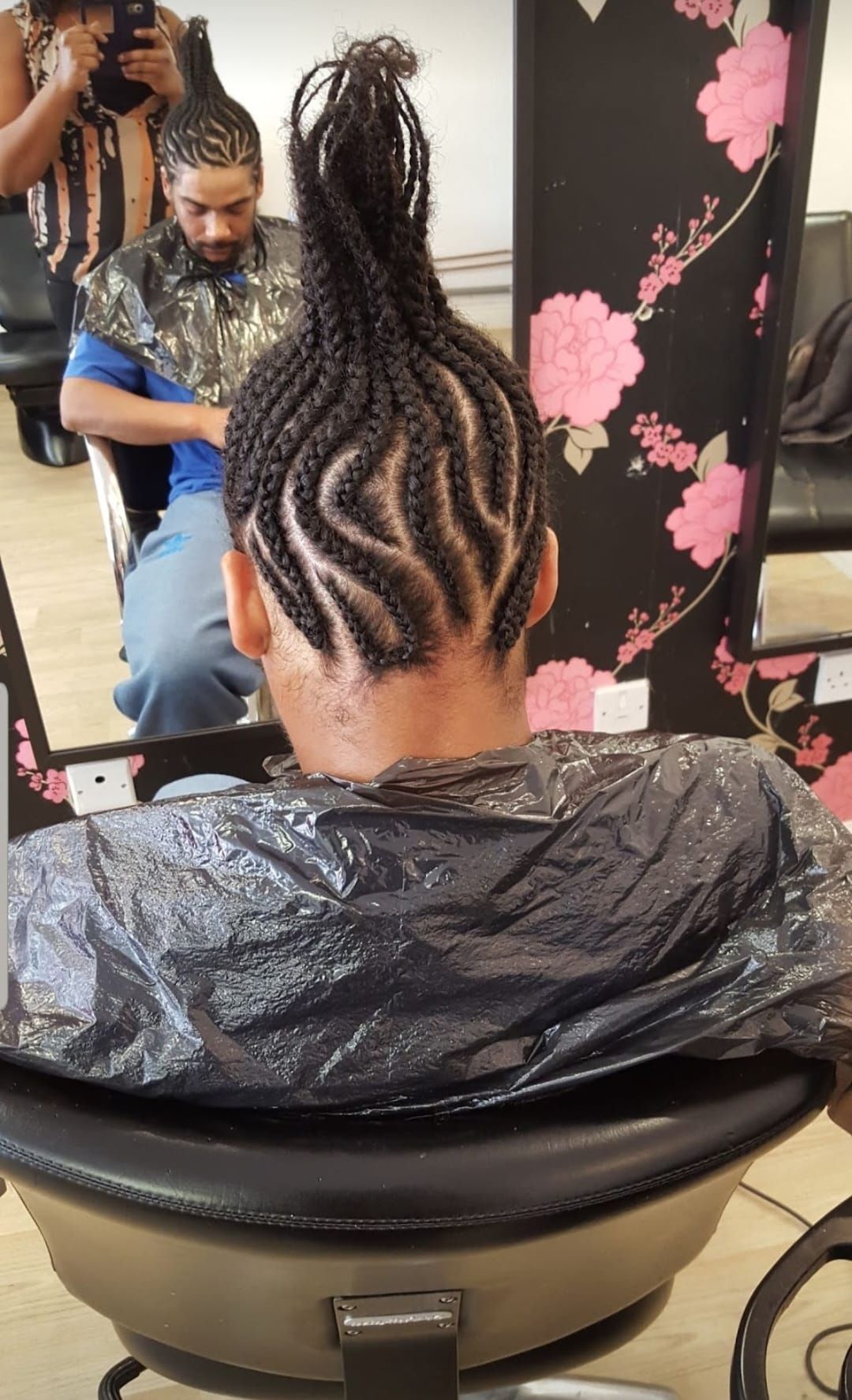 Braided hair being styled in a salon chair, with a stylist working in front of a mirror.
