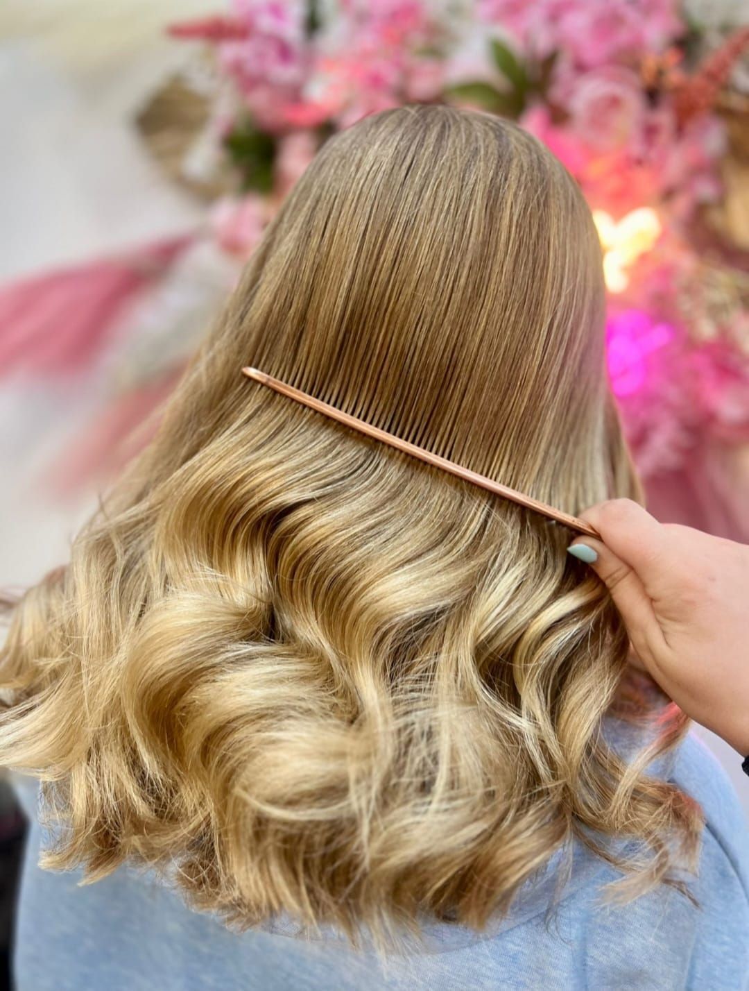 Woman showing long blonde wavy hair being combed against a pink floral background