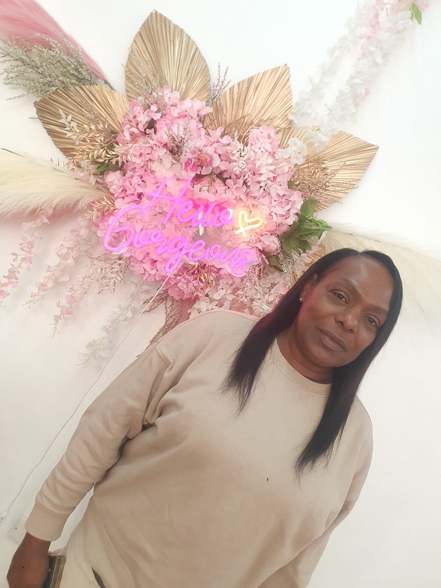 Person standing indoors against a floral wall display with pink and gold decorations.