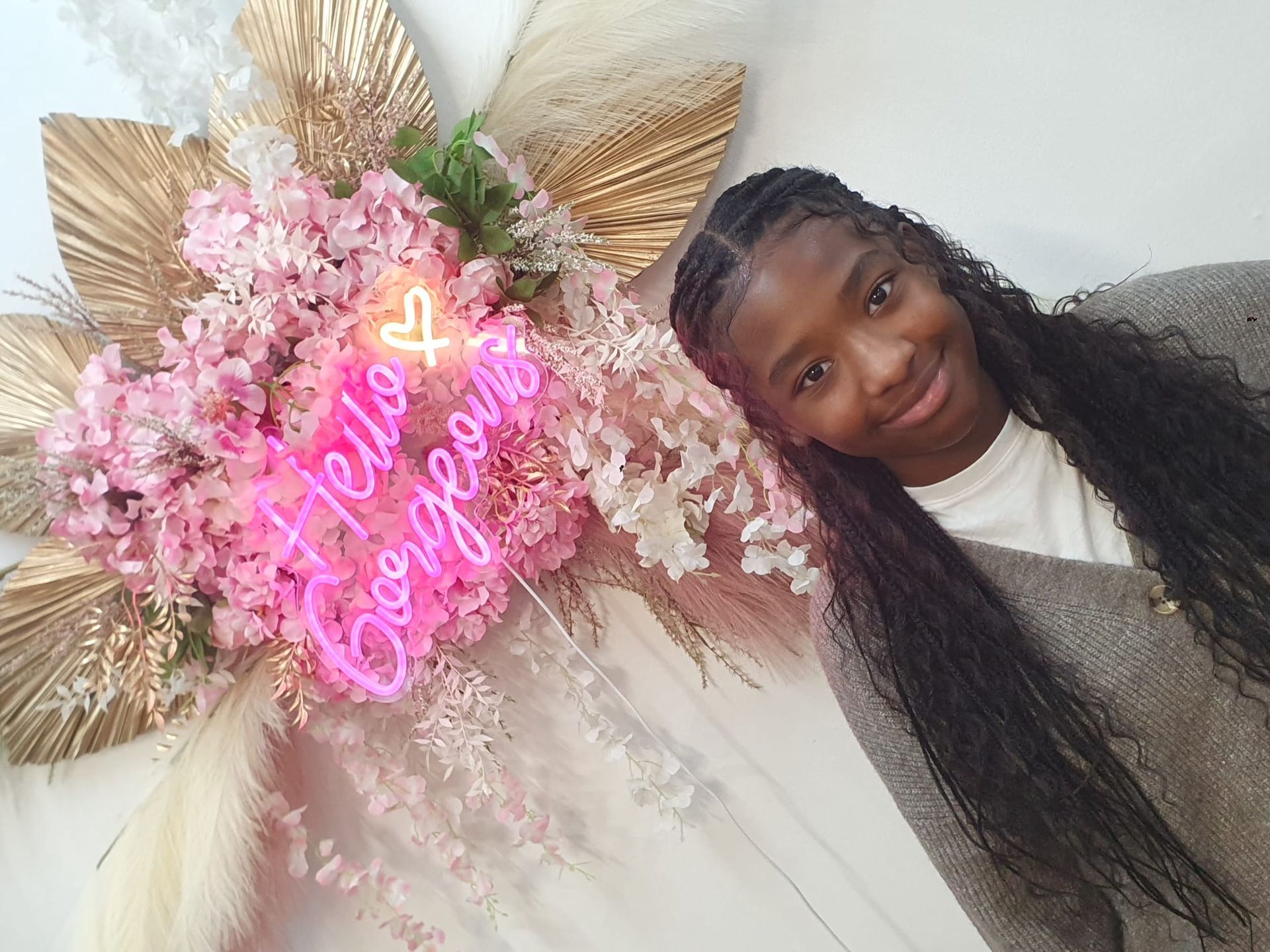 Woman smiling beside pink floral neon wall decor with gold palm leaves