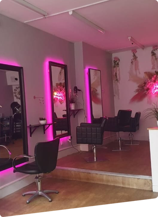 Salon interior with pink neon-lit mirrors, black chairs, and a wooden floor