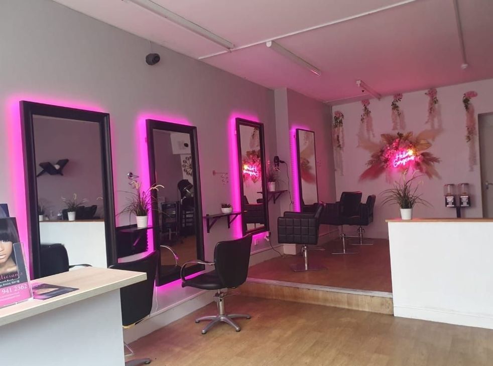 Pink-lit hair salon interior with styling chairs, mirrors, and a white reception counter