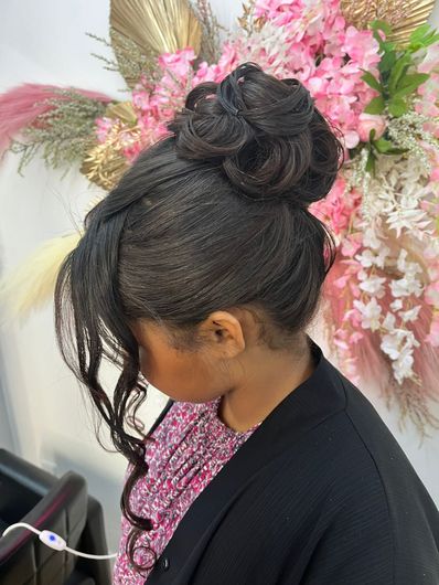 Woman with a braided updo and pink top standing before a pink floral backdrop