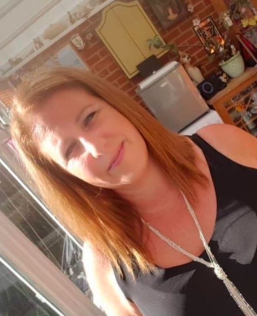 Woman posing in a sunlit kitchen, wearing a black top and necklace.