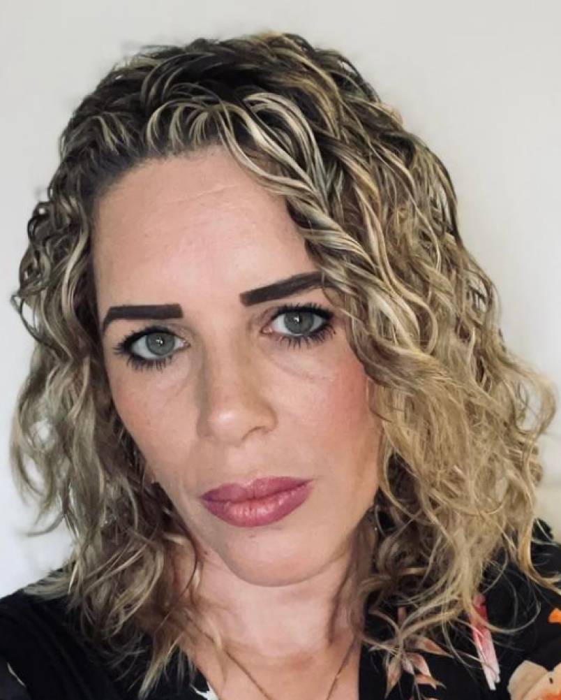 Close-up portrait of a woman with curly blonde hair and pink lipstick, looking at the camera.