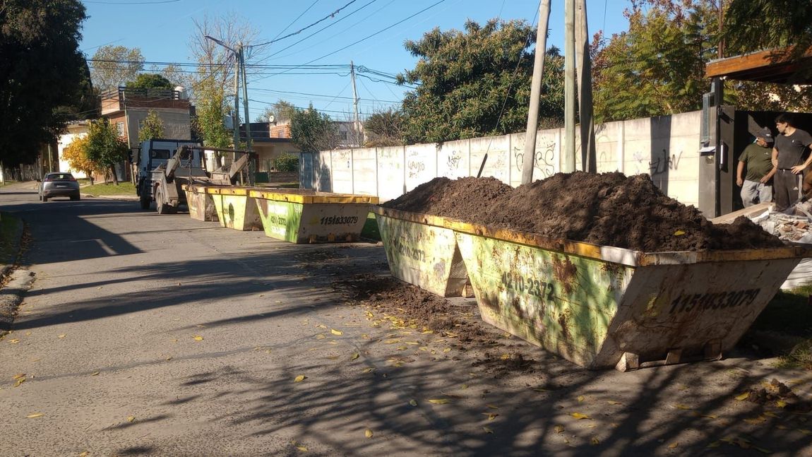 Una retroexcavadora amarilla estacionada junto a un muro de chapa ondulada en un patio industrial.