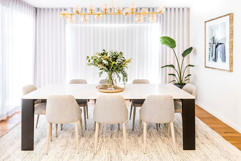A dining room with a table and chairs and a vase of flowers on the table.