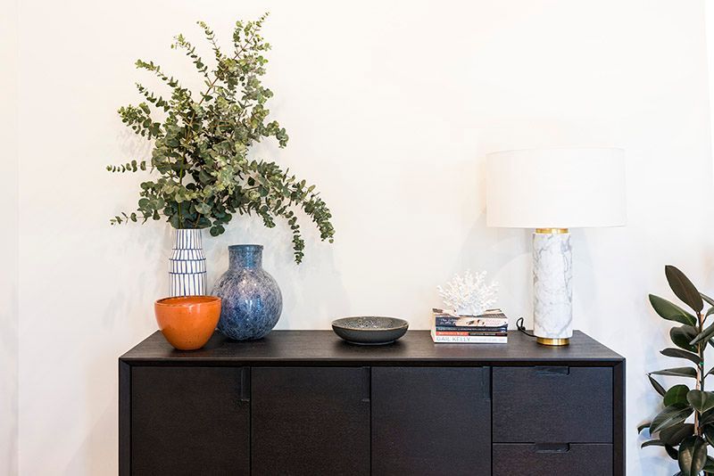 A black dresser with vases and a lamp on it.