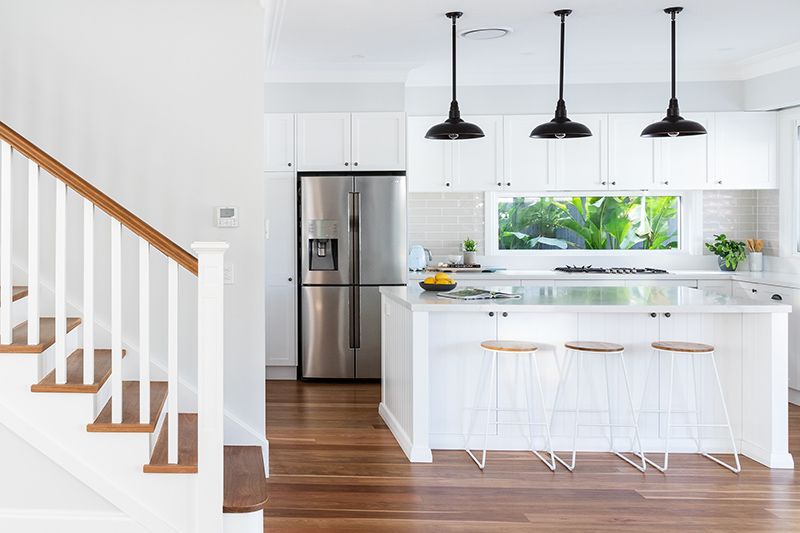 A kitchen with white cabinets and stainless steel appliances and a staircase leading to the second floor.