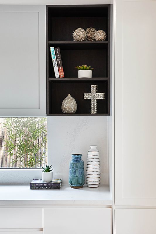 A shelf with vases and a cross on it next to a window.